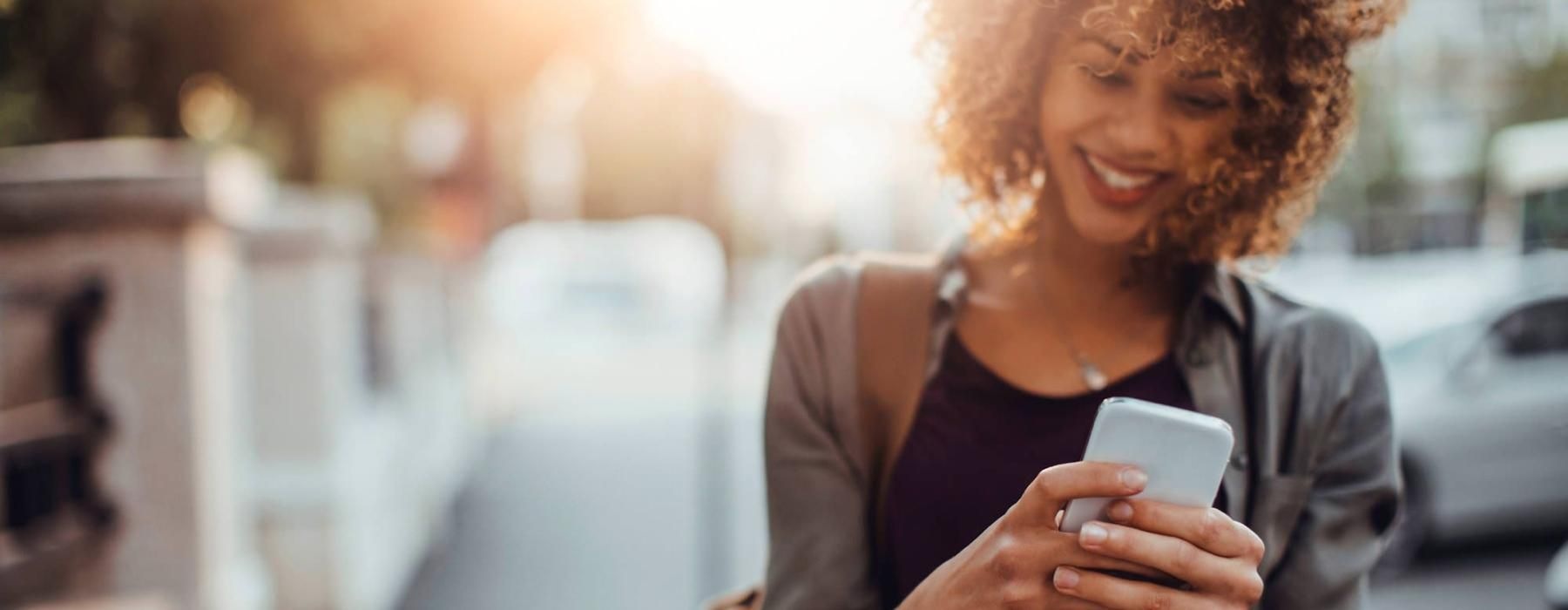 woman texts on her phone as she walks through the city